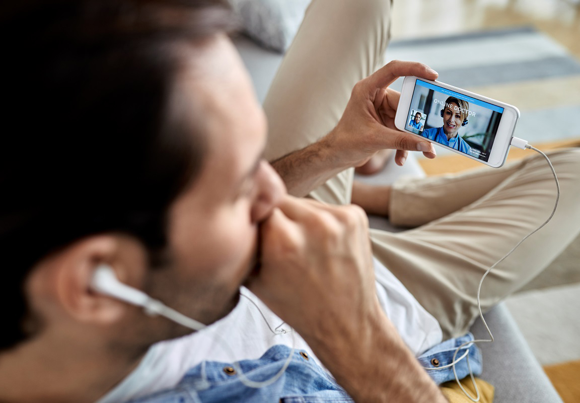 Close-up of man man coughing while using smart phone and talking online with his doctor from home.