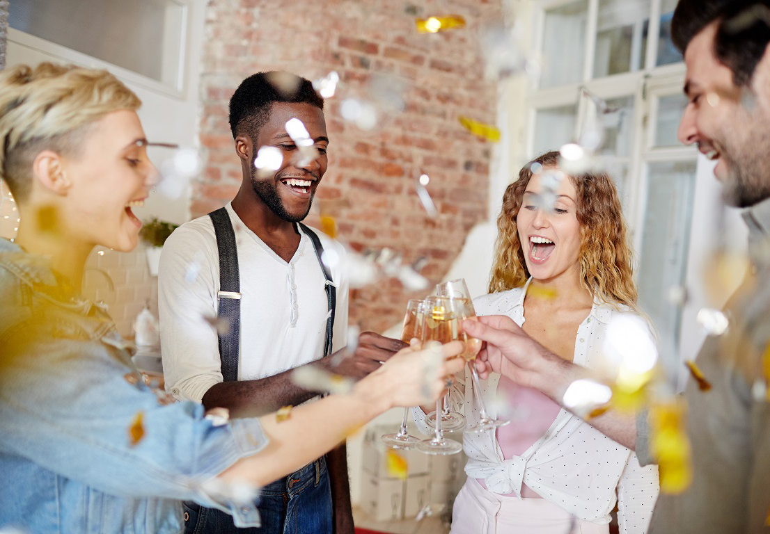 Ecstatic girls and their boyfriends clinking with champagne flutes in confetti fall